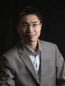 Short hair Asian man in eyeglasses wearing a grey suit with a light grey shirt