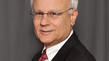 head shot of balding man with white hair and eyeglasses wearing a dark brown suit, white shirt, and maroon patterned tie