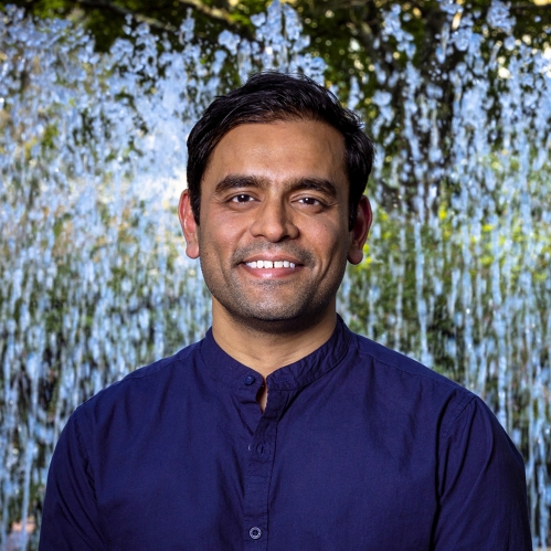 Headshot of male with short black hair wearing a dark blue button down shirt.