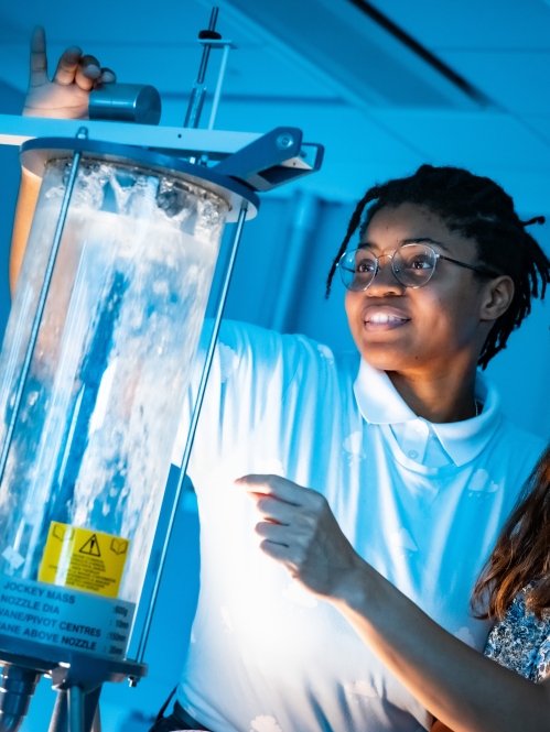 Two female students looking at a vessel holding water. The room is lit blue.