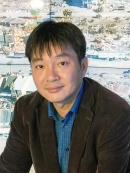 head shot of Asian male with sort black hair wearing a brown suit jacket and blue patterned shirt