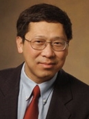 head shot of asian male wering eyeglasses with short dark hair wearing a black suit, maroon tie, and light blue shirt