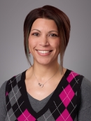 Headshot of female with short hair wearing a pink and black argyle sweater over a long grey sweater.