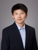 Headshot of female with short black hair and black post earrrings, wearing a light blue button down shirt and black jacket.