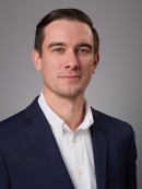 Headshot of male with short hair wearing a white button down shirt and a dark suit jacket.