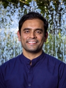 Headshot of male with short black hair wearing a dark blue button down shirt.
