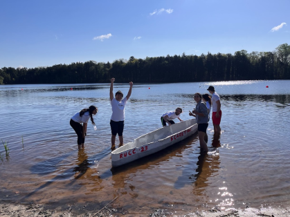 Civil engineering students pose with their concrete canoe in shallow lake water.