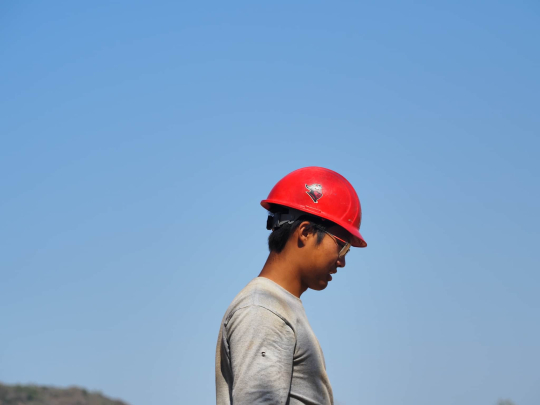 Student wearing red Rutgers hardhat standing against a blue sky