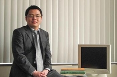 Photo of Dr. Hao Wang sitting on a desk with a computer to his left