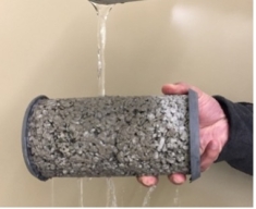 Hand holds a concrete cylinder under running water.